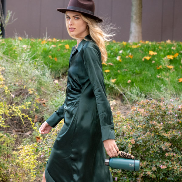Az utcán sétáló nő, kalapban és kulaccsal a kezében